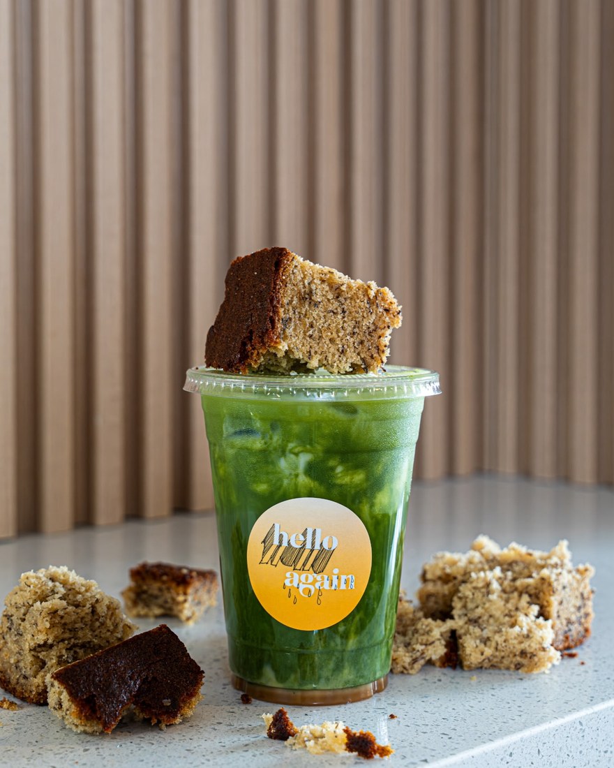 An iced matcha in a Hello Again cup with a slice of coffee cake
